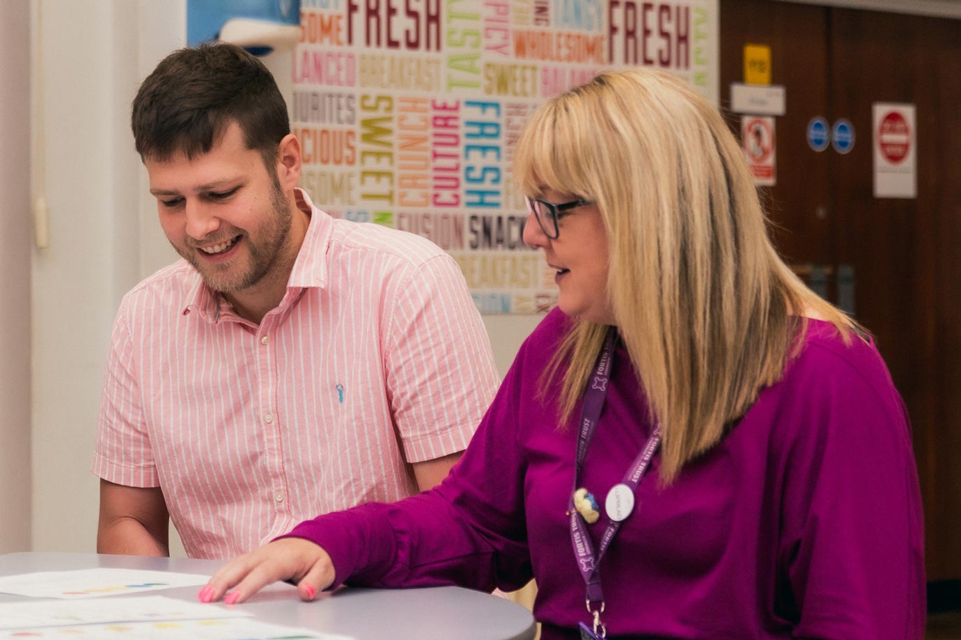 An Outreach practitioner providing training. She is speaking and pointing at a piece of paper. A male staff member is looking at the paper, smiling.